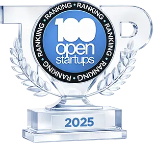 Troféu transparente com selo '100 Open Startups 2025', reconhecendo empresas entre as mais bem posicionadas no ranking de inovação aberta e conexão com startups.